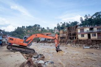 An excavator machine is falling into rushing water through the center of a village in Nepal due to flooding from climate change. © UNICEF/UNI655366/Upadhayay