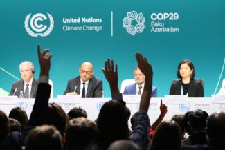 Participants of the UN Climate Change Conference 2024 raise their hands
